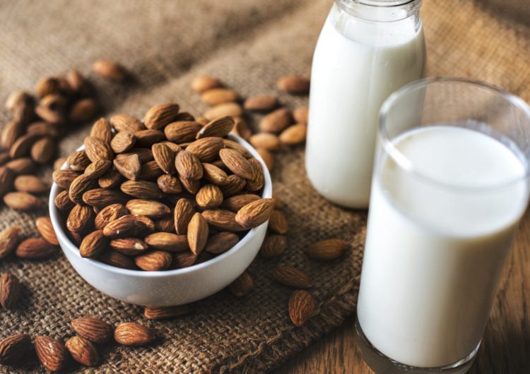 A white bowl of almonds and a glass of Almond milk