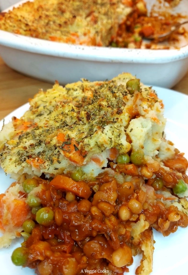 Portion of vegan shepherd’s pie on a white plate with rest of pie in the background