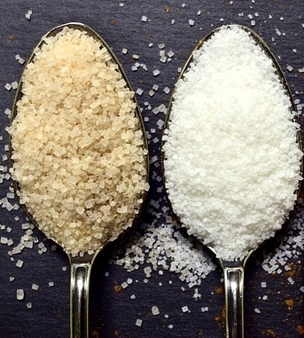 A spoon with white sugar and a spoon with brown sugar